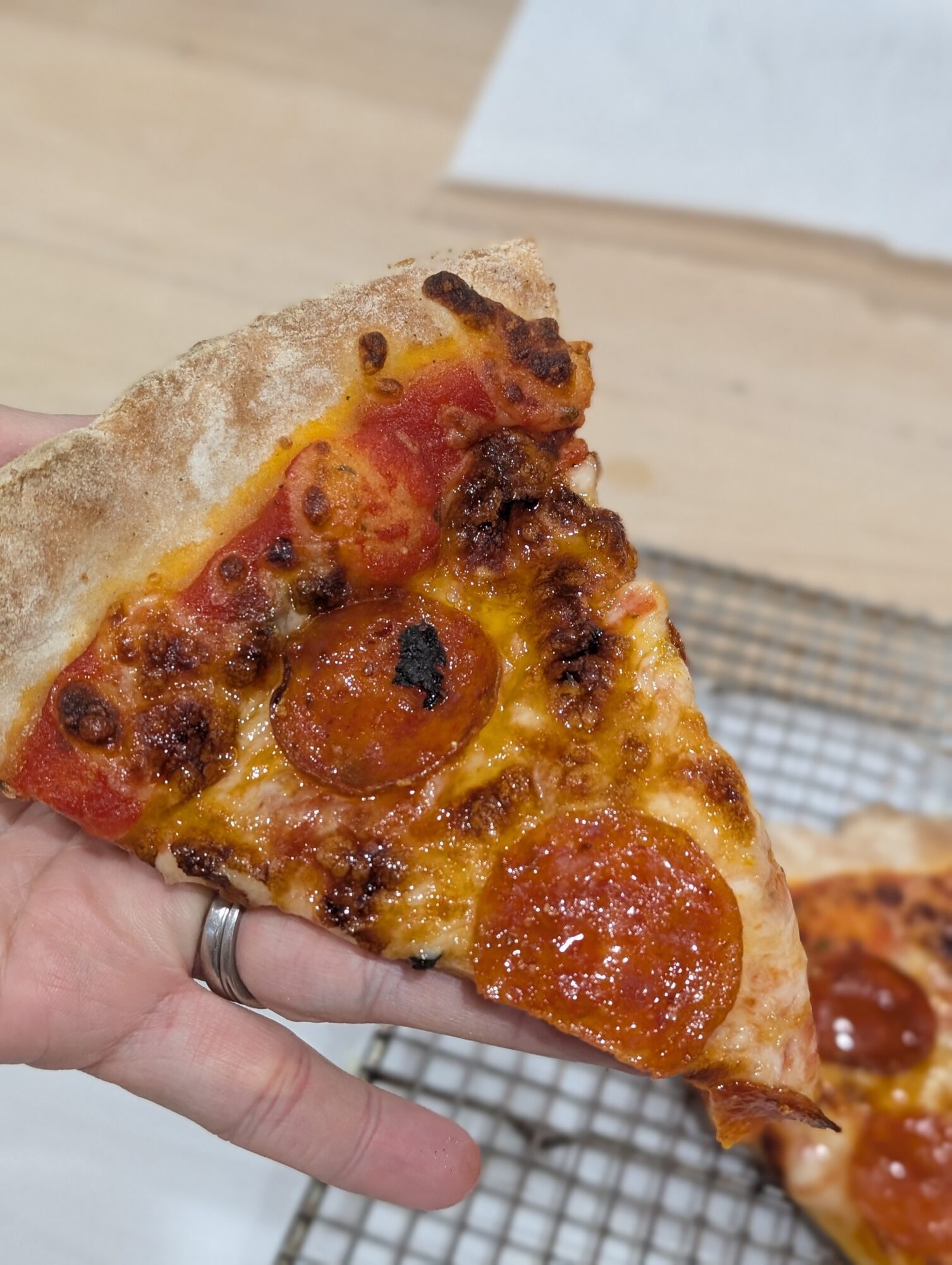 Close-up of a hand holding a slice of pepperoni pizza with melted cheese and toppings, with a pizza box in the background.
