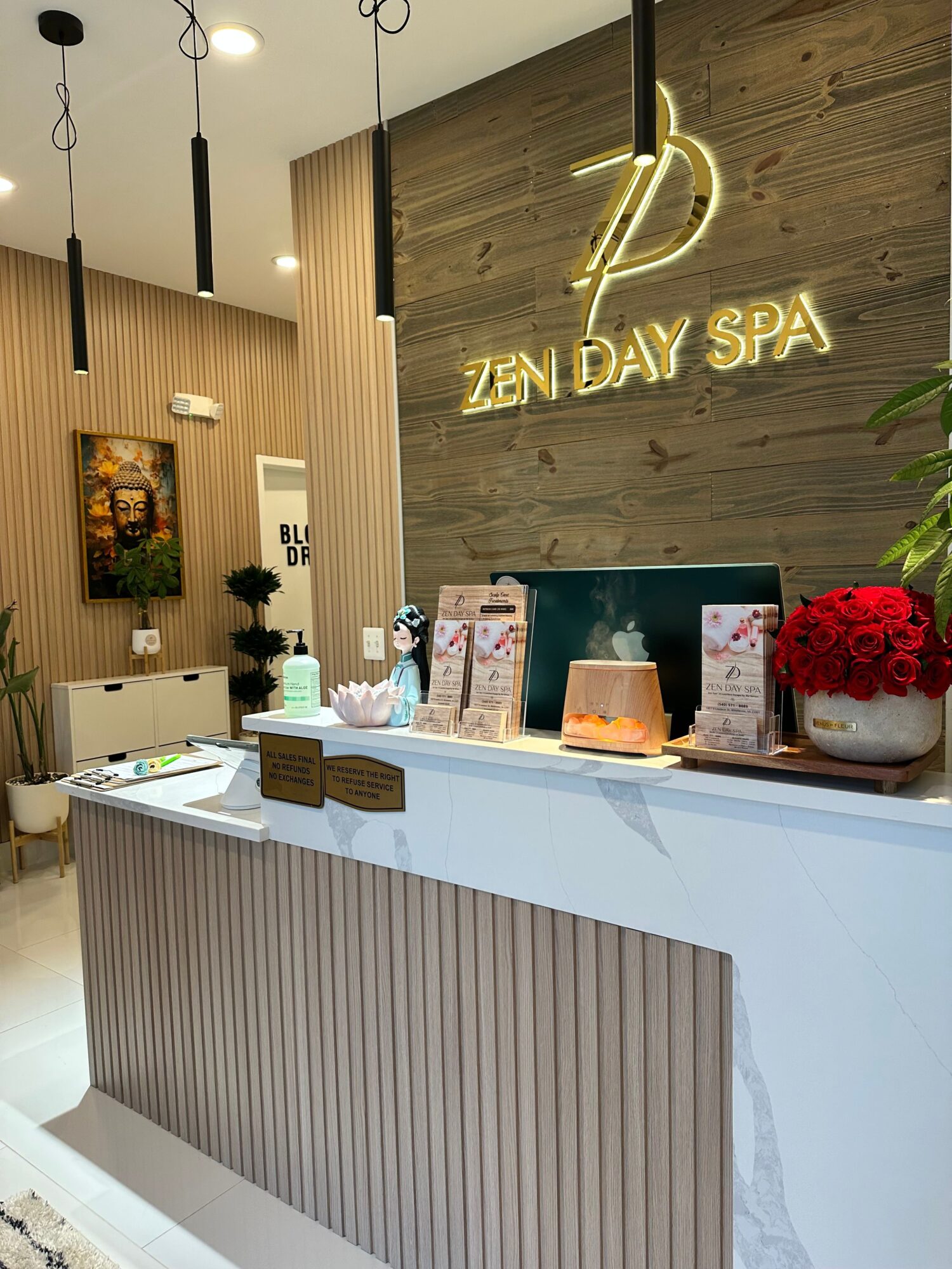 Spa reception area with a neon sign, flowers, and product displays, viewed from a low angle.