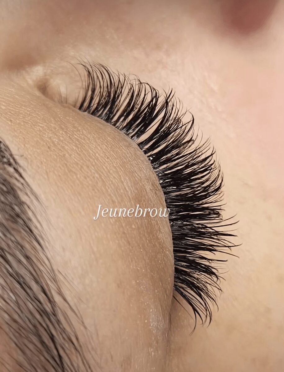 Close-up of a person's closed eye with long, thick eyelashes and smooth skin.