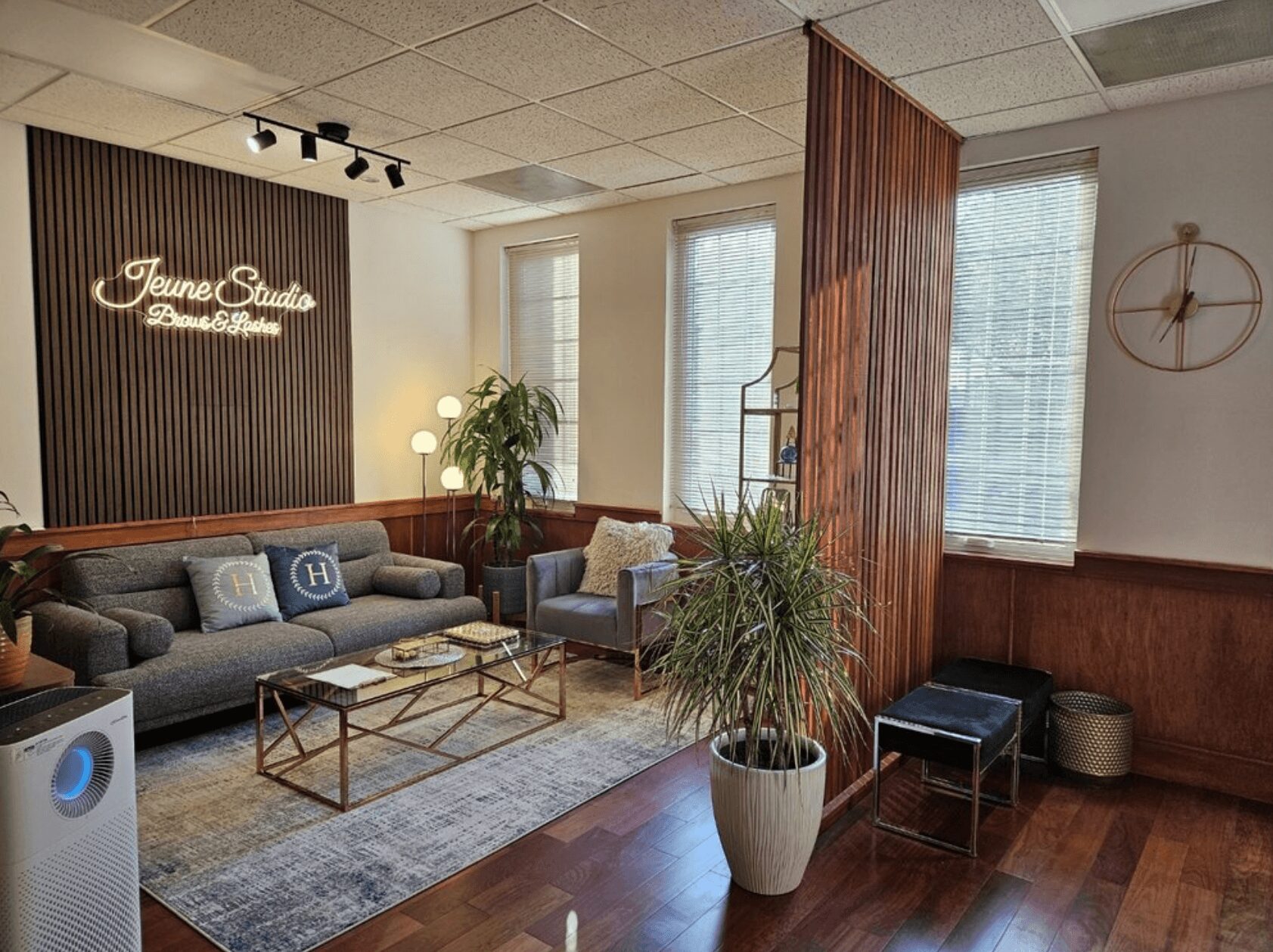 Modern lounge with sofa, plants, large windows, and a sign reading 'Jeune Studio' on the wall.