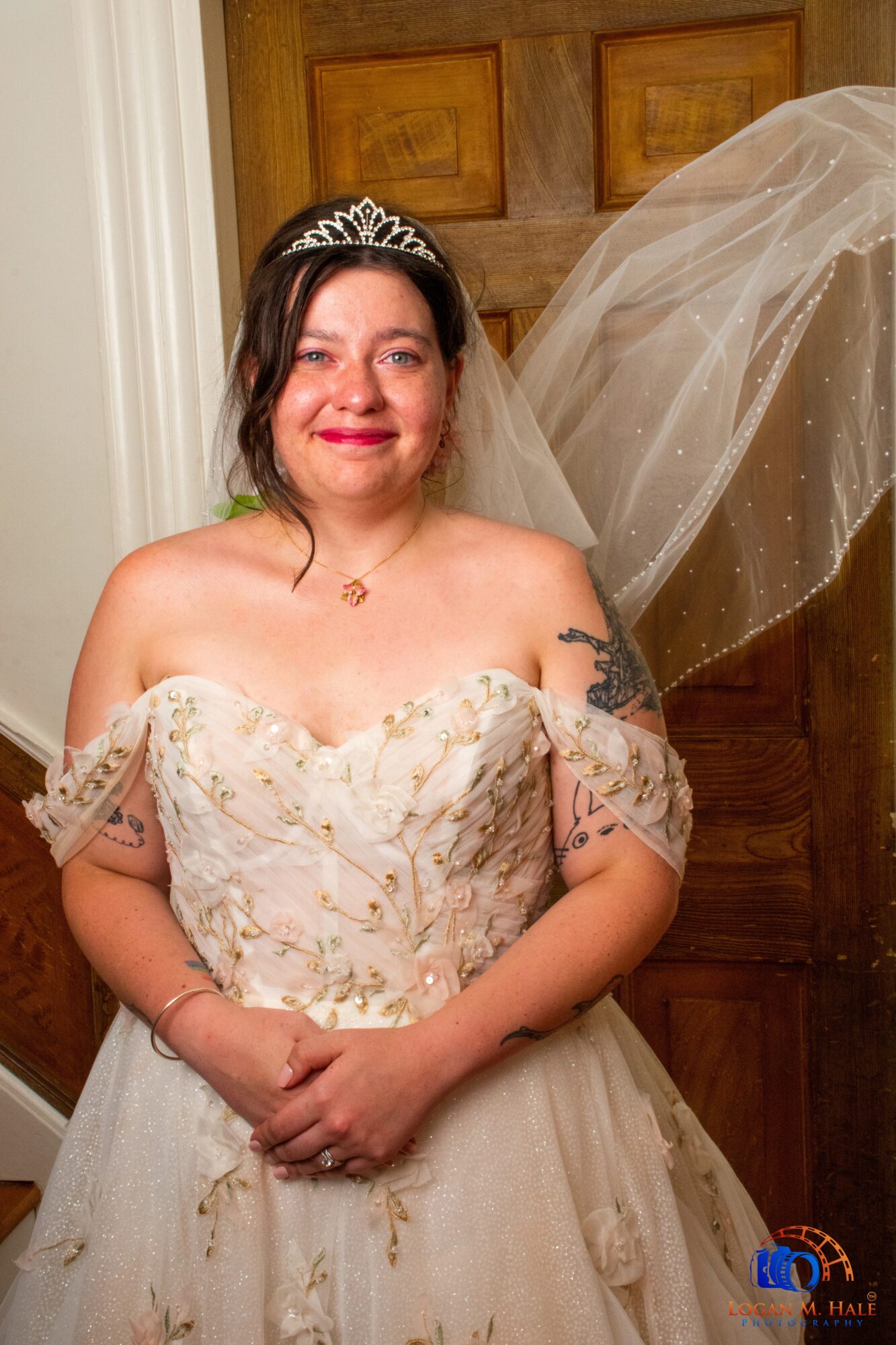 Woman in wedding dress with tiara and veil, smiling, standing indoors in front of wooden door.