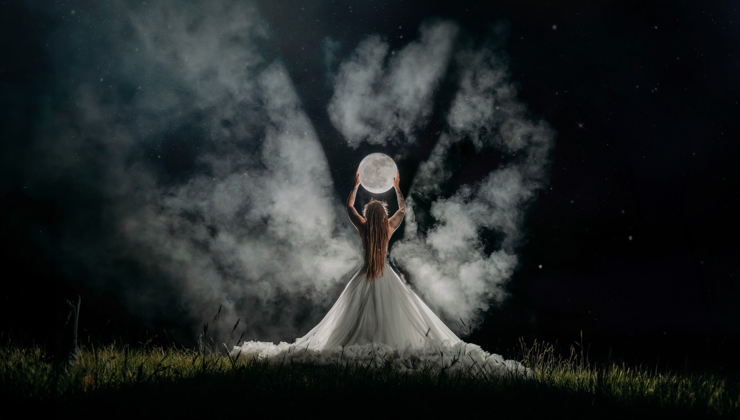 Person in a white dress holding a large moon-shaped object, standing on grass under a cloudy night sky.
