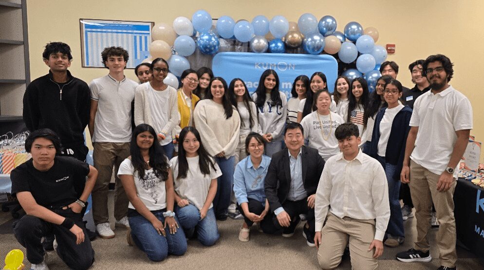 Group of young people and adults posing in front of blue and white balloon decorations indoors.