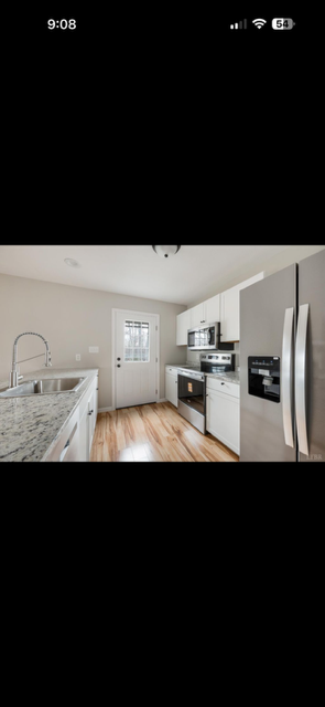 Kitchen with white cabinets, stainless steel appliances, and a wooden floor, with a door and window in the background.