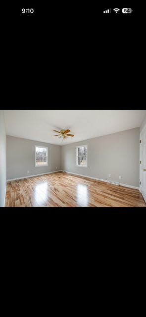 Empty room with hardwood floor, two windows, ceiling fan, and light gray walls.