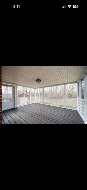 Enclosed porch with wooden floor, white railing, and large windows showing outdoor scenery.