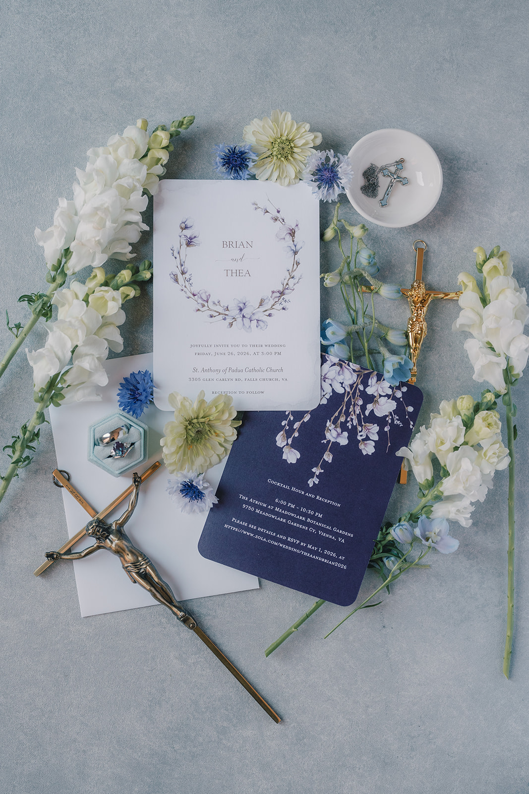 Flat lay of wedding invitation, flowers, candle, and sword on gray background.