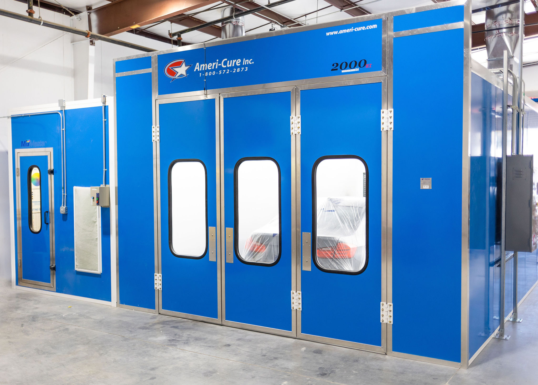 Blue industrial spray booth with windows and a sign reading 'Ameri-Cure Inc.' inside a warehouse.