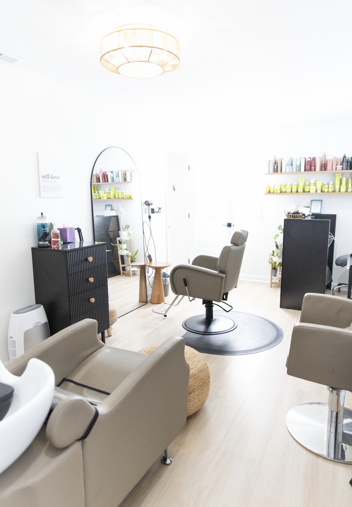 Salon with chairs, shelves, and a mirror, illuminated by a ceiling light, with light-colored flooring and bright walls.