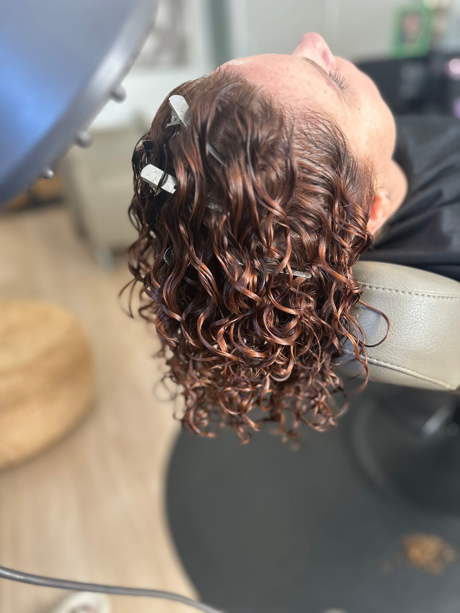 Person with curly hair lying back in a chair, head tilted to the side, hair styled in loose curls.