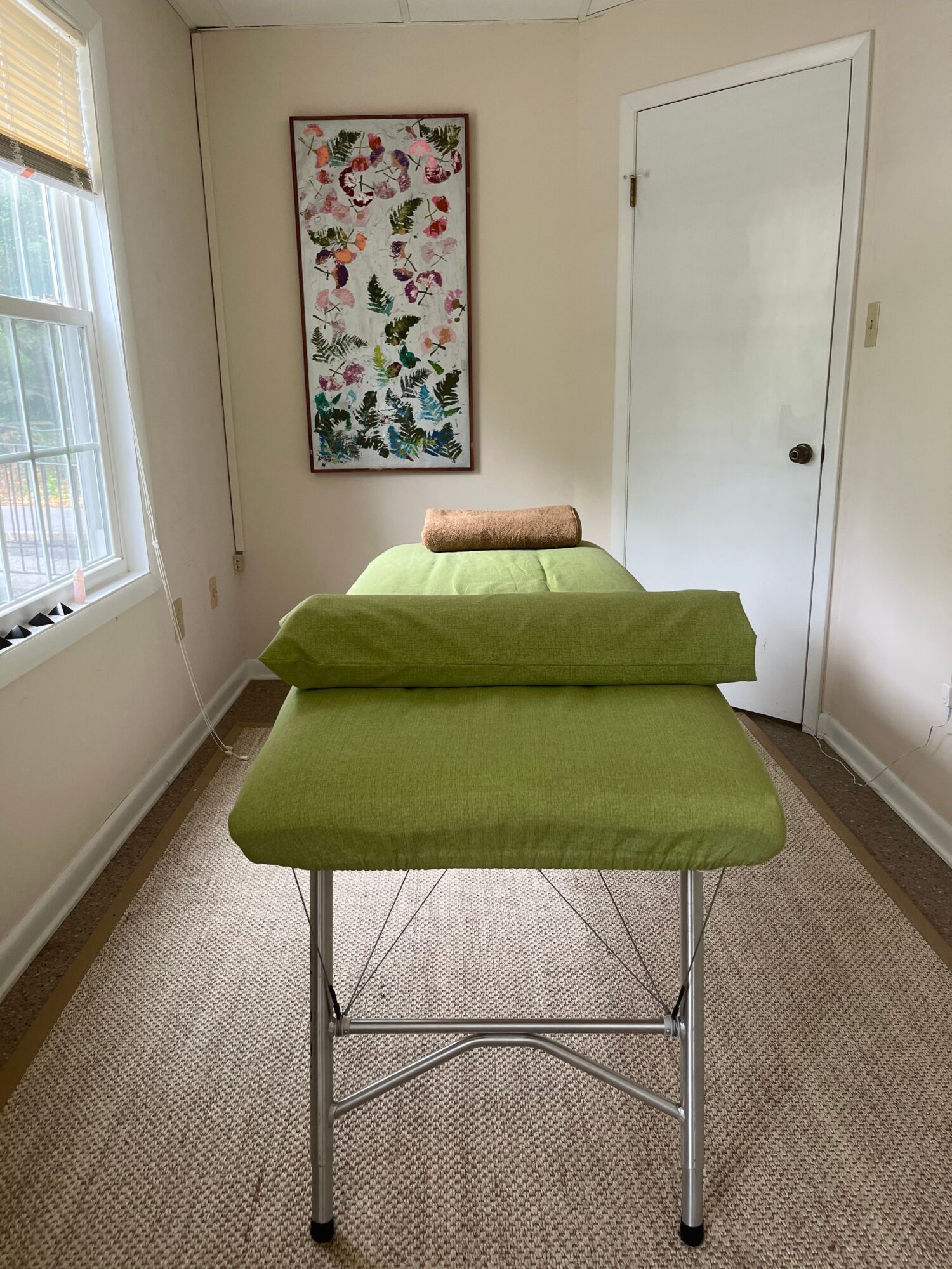 Green upholstered chair with a brown armrest in a room with a window and colorful artwork on the wall.
