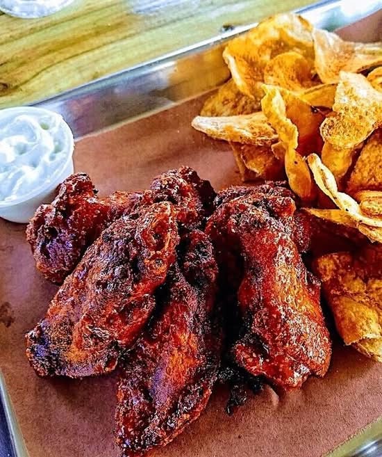 Barbecue chicken wings with potato chips and a dollop of white sauce on a tray.
