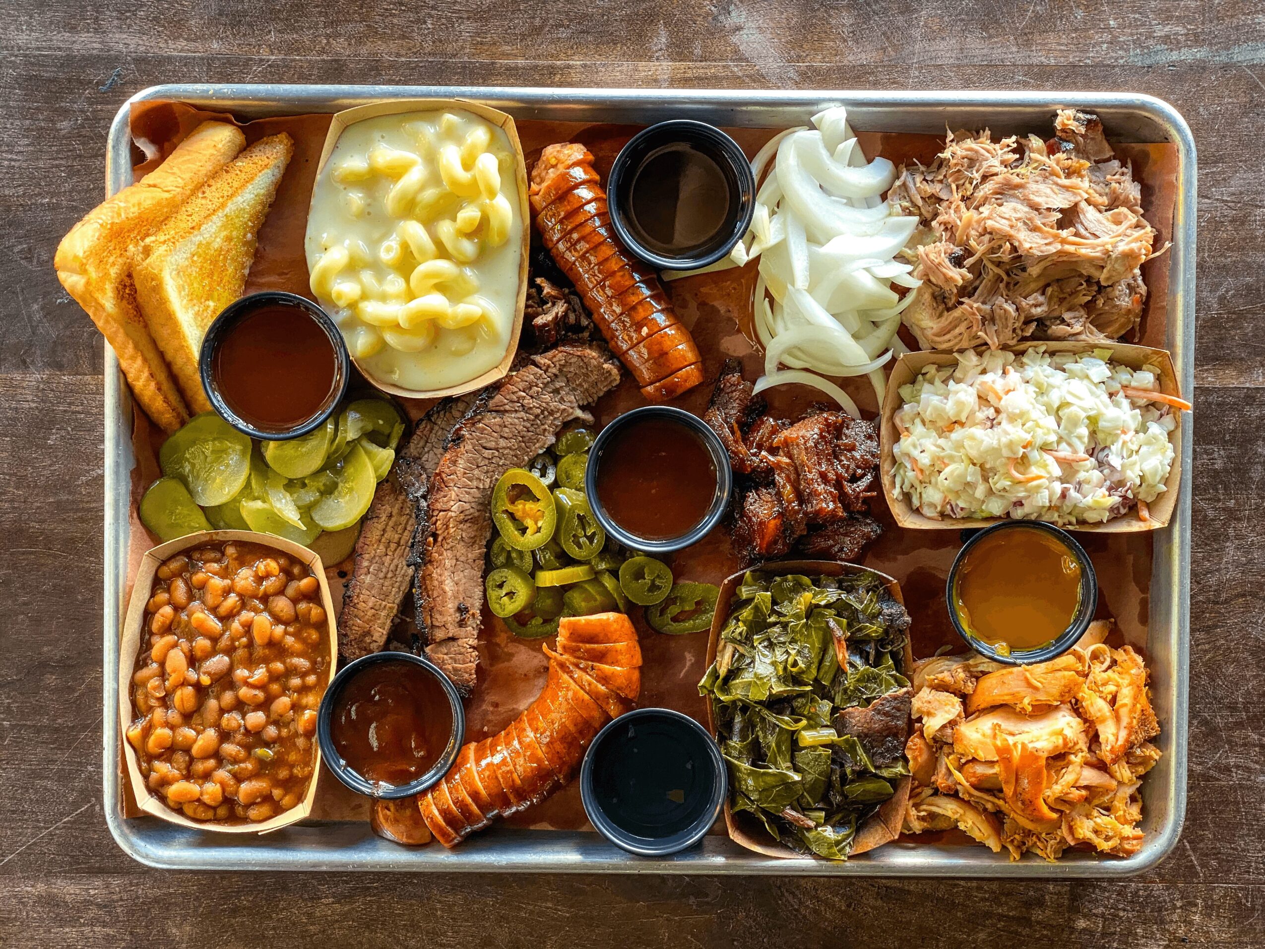 A tray with toast, cheese, sausage, pickles, baked beans, meat, vegetables, and sauces, arranged in sections.