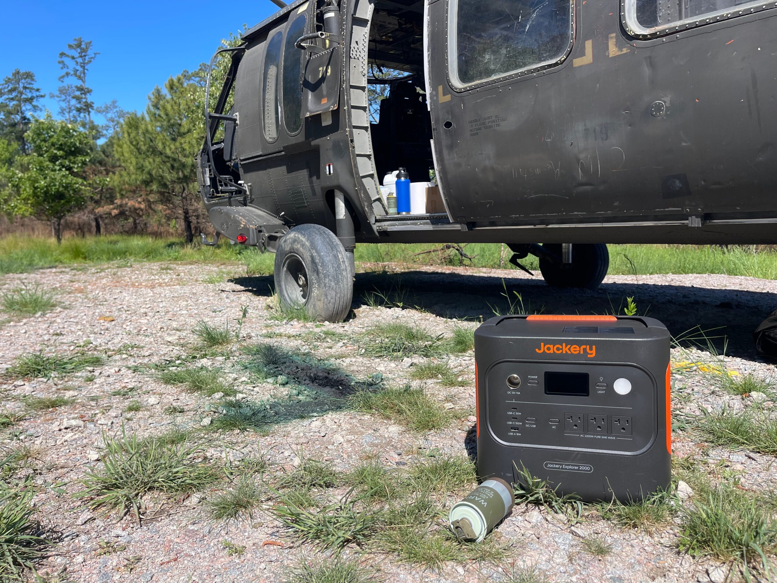 Black vehicle with open door and visible interior, parked on grassy area with trees in background, device on ground nearby.