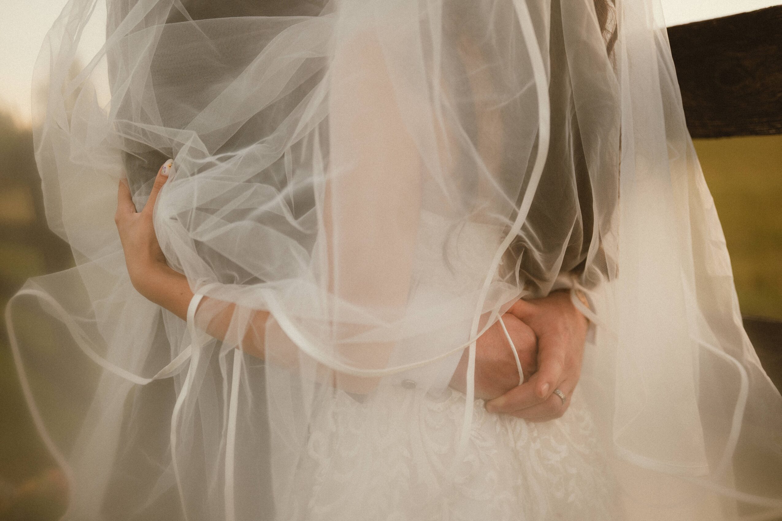 Close-up of a person in a wedding dress with sheer fabric, holding a small child in a similar dress, indoors.