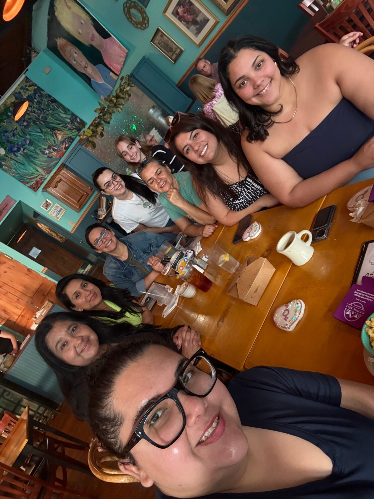 Group of people smiling and sitting at a table in a restaurant, with colorful decor and framed pictures on the wall.