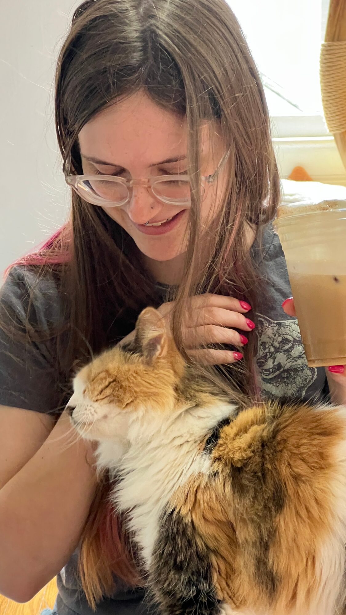 Person with glasses smiling, holding a fluffy calico cat, in a cozy indoor setting.